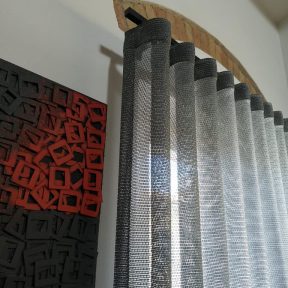 Il rosso e nero di un ambiente a piani e il grigio grafite della tenda in tessuto di rete metallica. Le tende di Mariano, Verona, Lessinia, Genova, Veneto, Liguria, Italia.